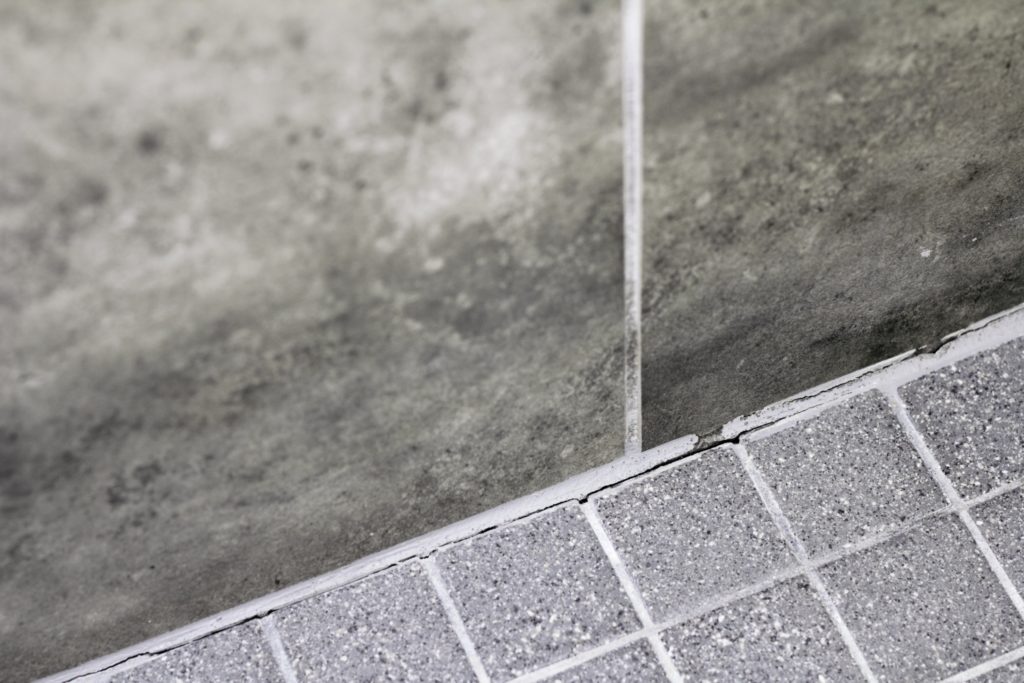 A shower enclosure with cracked grout on gray tile.