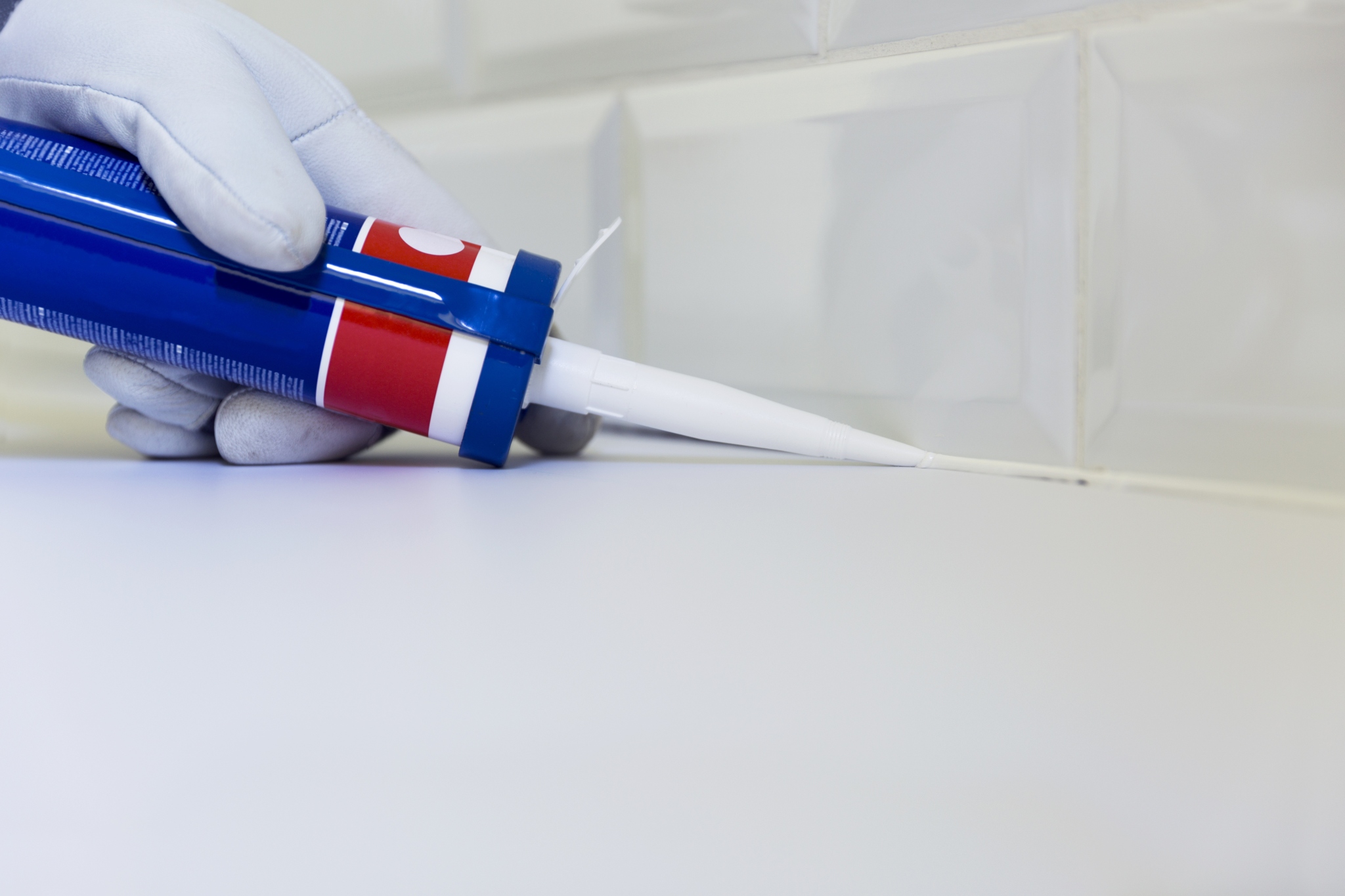 A technician fufulling hotel maintenance duties by replacing caulk in a hotel bathroom.