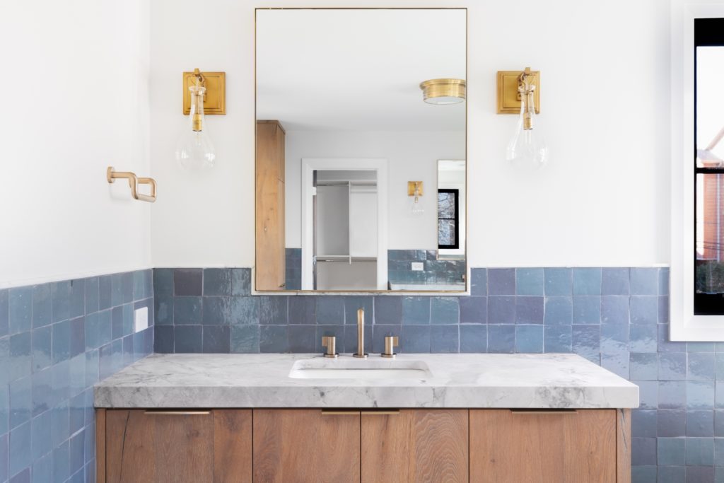 A hotel bathroom with a marble vanity top and a blue tile backsplash. 