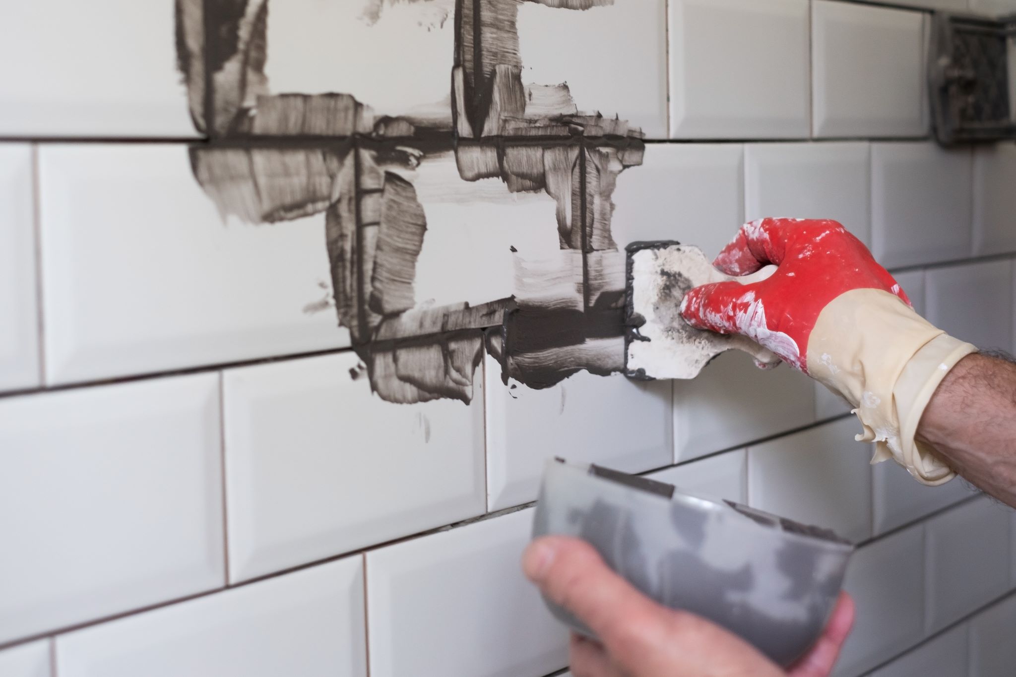 A professional grout sealing white tile with a gray sealant