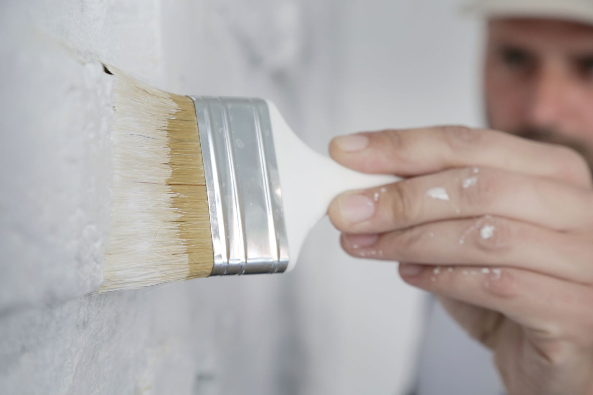 painting a white wall with a paint brush using a low VOC formula paint